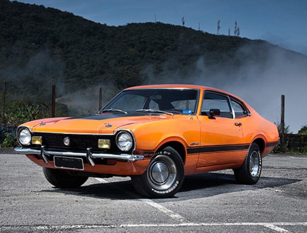 Ford Maverick GT brasileiro de 1974, laranja com faixas pretas, estacionado numa estrada de serra.